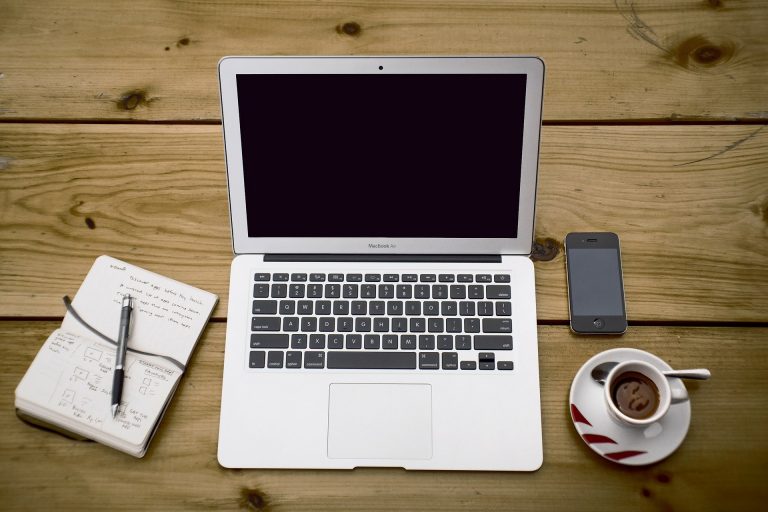 Laptop on table with coffee, phone and notepad